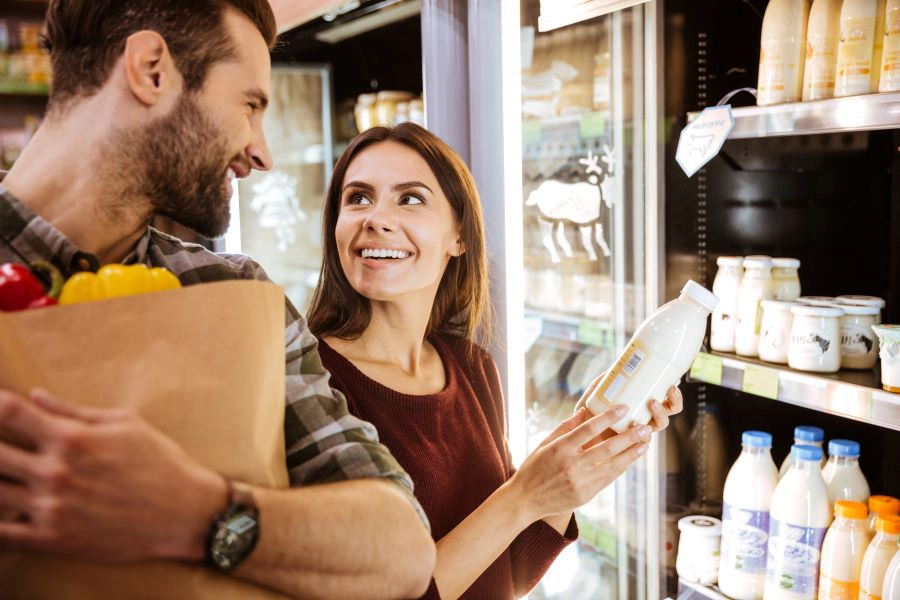 woman holds milk bottle and smiles at man doing groccery shopping